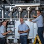 3 men in front of industrial electrical controls 