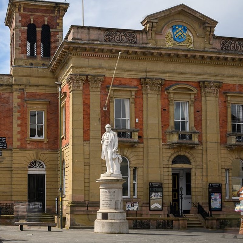 Image shows town hall brick building with statue in front