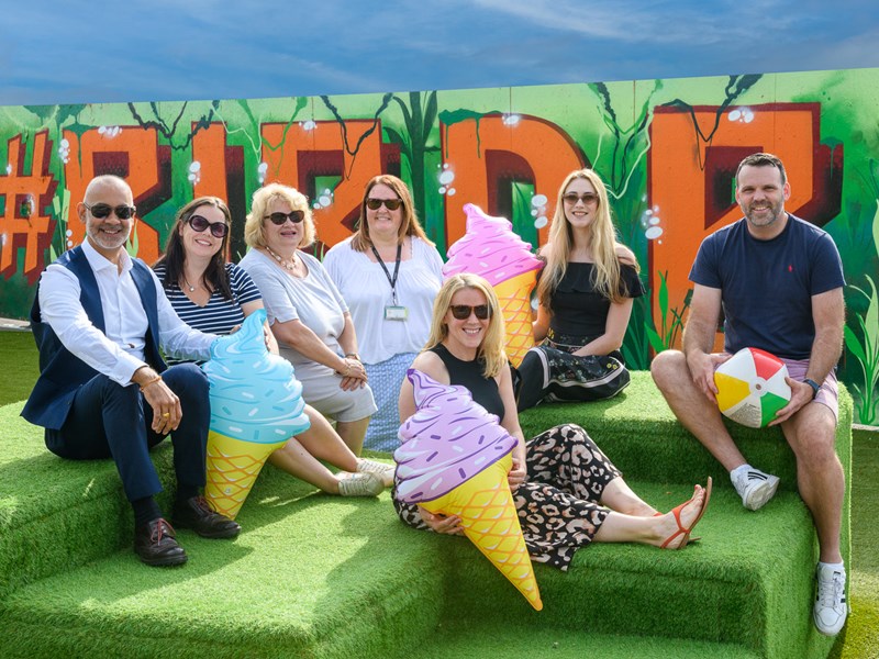 7 people in summer outfits sat on green grass style boxes
