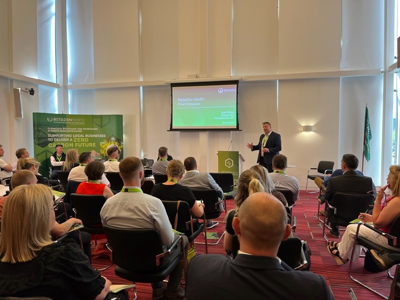 People seated in a meeting room with person presenting at the front of the room